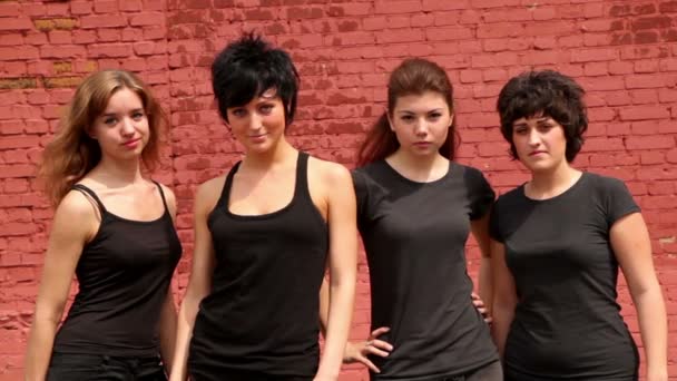 Четыре девушки смотрят и улыбаются, на фоне красной стены — стоковое видео