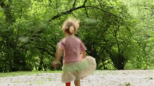 Girl hopping and runs away across meadow all strewn fluff, then she stops and touch her nose — Stock Video