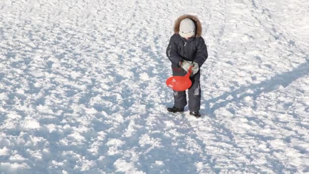 Boy with sled rises to snowy hill, falls, climbs and finishes ascent — Stock Video