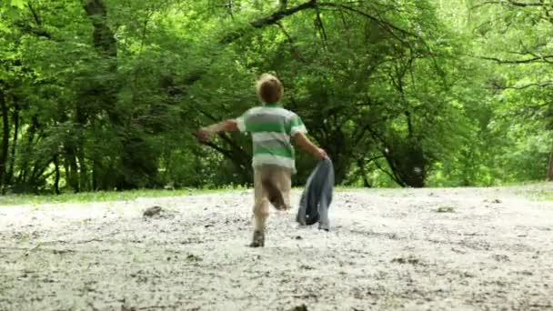 Boy runs, then he stops and runs back across meadow all strewn fluff — Stock Video