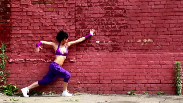 Гнучка дівчина танцює біля стіни з червоної цегли — стокове відео