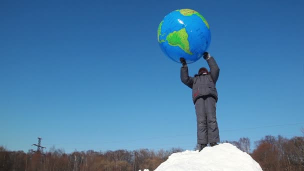 Boy stand on snow pile and hold inflated ball over head, then he throws it — Stock Video