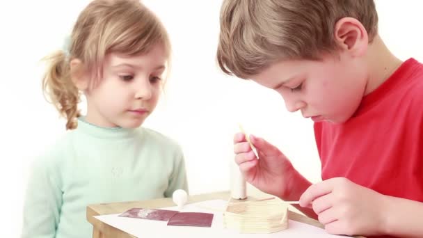 Girl watch on how boy apply glue on stick and attach to wall of match house — Stock Video