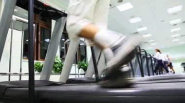 bir büyük salonunda birçok koşu bandı üzerinde çalışan bacaklar adam