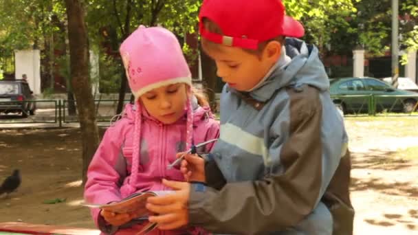 Мальчик и девочка сидят вместе и смотрят журнал — стоковое видео
