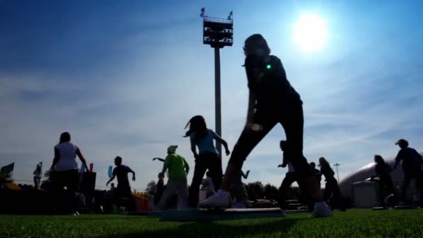 Siluete de oameni angajați în exerciții aerobice pas pe stadion — Videoclip de stoc