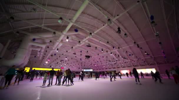 As pessoas patinam na pista de gelo com iluminação colorida — Vídeo de Stock