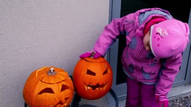Маленькая девочка смотрит на две головы тыквы на Хэллоуин — стоковое видео