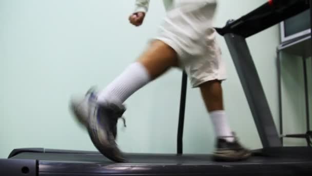 Nohy člověka jít na běžeckém pásu poblíž zdi v tělocvičně — Stock video