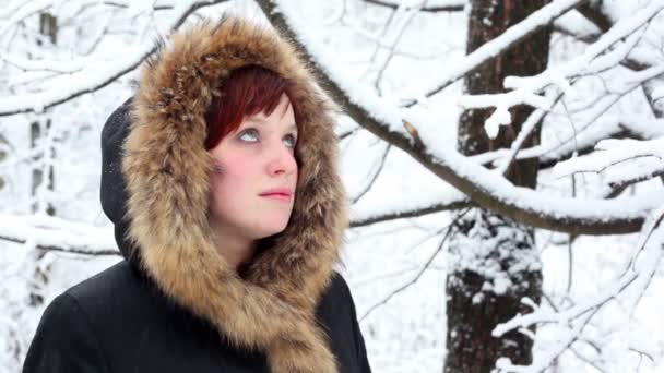 Chica en capucha de piel mira la nieve cayendo — Vídeos de Stock