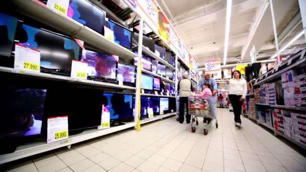Семейная прогулка возле витрины с множеством телевизоров в гипермаркете Auchan — стоковое видео