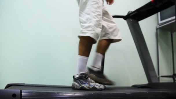 Benen van man komen op loopband in de buurt van muur in sportschool en beginnen ga — Stockvideo