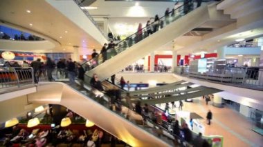 birçok kişi birden fazla katlı alışveriş merkezi atrium içinde yürüyen merdiven üzerinde hareket