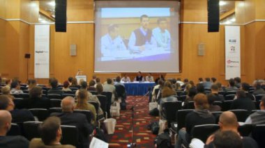 Lee torrens konuşuyor, masada oturan ve büyük ekranda gösterilen