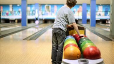 küçük çocuk bowling topları alır ve bovling yenmek için atar
