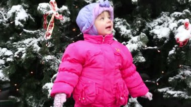 küçük kız duruyor ve karla kaplı Noel ağacı önünde doğru bak