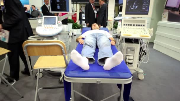 Pasien terbaring di tempat tidur, jantungnya ditunjukkan pada layar alat diagnostik ultrasonik di pameran medis — Stok Video