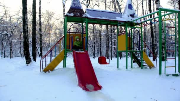 Girl sits on construction at childrens playground and slide down — Stock Video