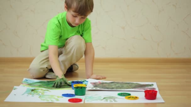 Boy draws color paints with his palm and fingers on sheet — Stock Video