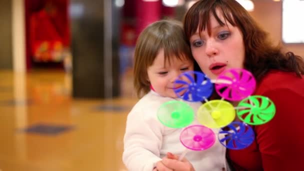 Filha sentar-se de joelhos mães, eles sopram no brinquedo fã — Vídeo de Stock