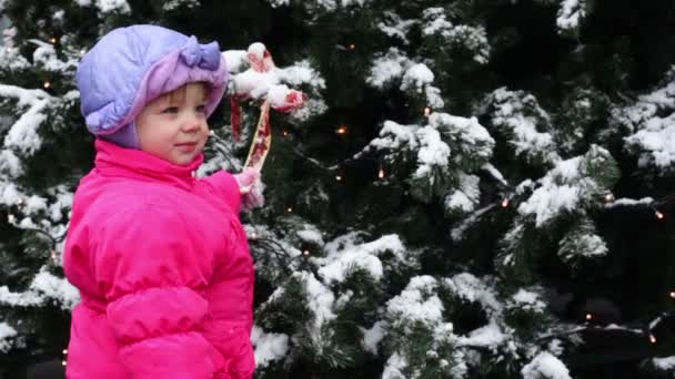 Dívka stojí a drží luk stuha na vánoční stromeček, pokryté sněhem — Stock video