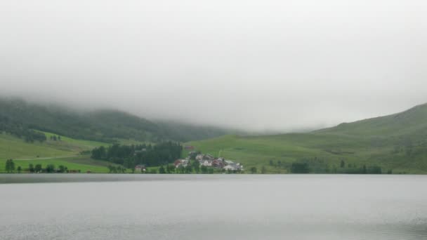Lago tranquilo frente a montañas cubiertas de niebla — Vídeos de Stock
