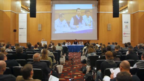 Lee Torrens speaks sitting at table and it is shown on big screen — Stock Video