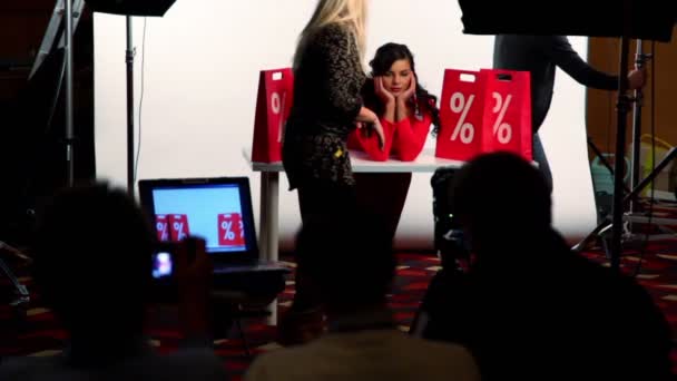 Modellen sitter vid bord bland plattor med procent tecken på demonstration av studio fotografering — Stockvideo