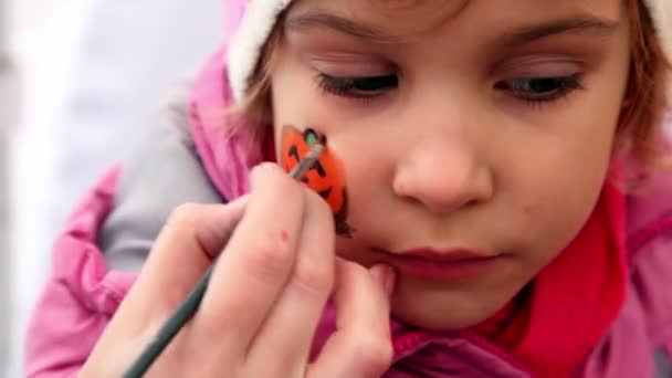 Рука держать кисть и рисовать тыкву на щеке девочек — стоковое видео