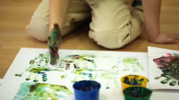 Little boy sits floor and leaves on paper handprints — Stock Video