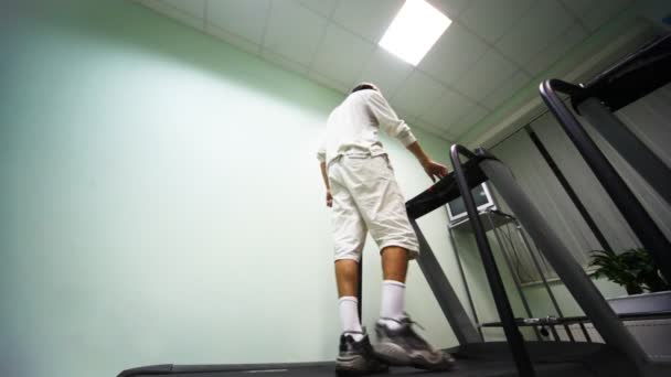 Homme debout au tapis roulant dans la salle de gym, il allume et commence à aller — Video