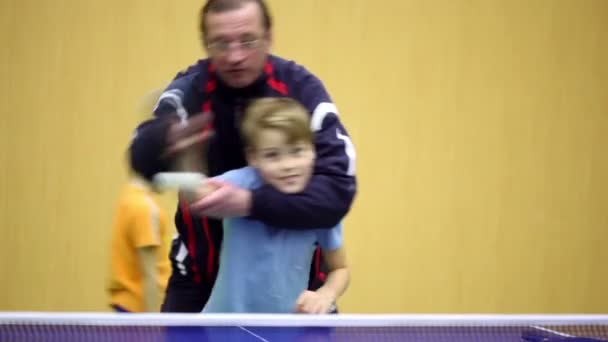 Тренер стоит позади, держит мальчика и учит его играть в настольный теннис — стоковое видео