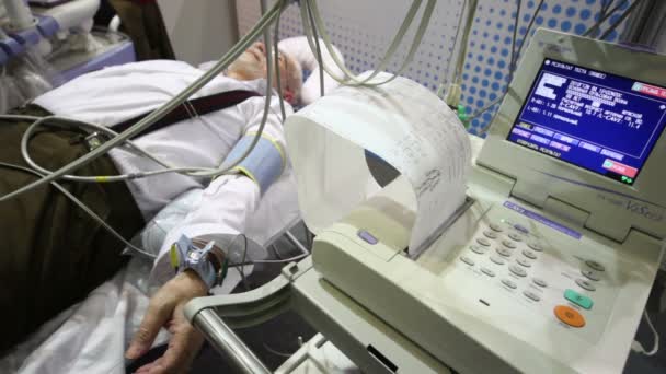 Elderly man lying on bed among medical diagnostic equipment at medical exhibition — Stock Video