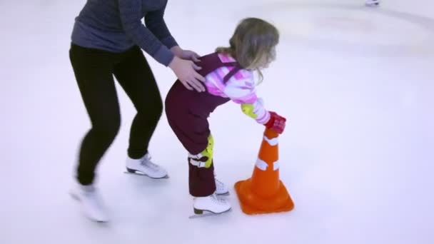 Mother push little girl on skates to ice rink border — Stock Video