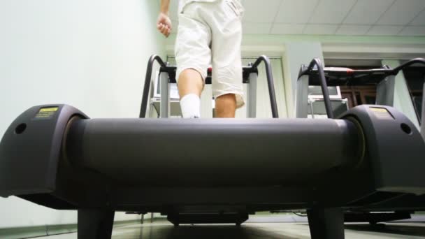 Jambes de l'homme debout au tapis roulant dans la salle de gym vide — Video