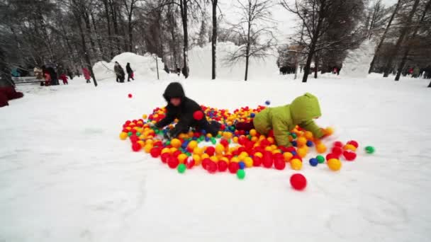 Boy and little girl play in pile of colored balls in park — Stock Video