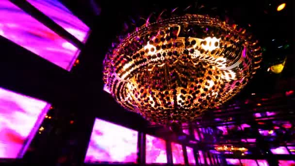 Kroonluchter en muur van monitoren ritmisch knipperende gekleurde lichten in nachtclub — Stockvideo
