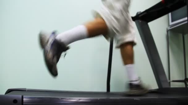 Ноги человека быстро бегают по беговой дорожке возле стены в тренажерном зале — стоковое видео