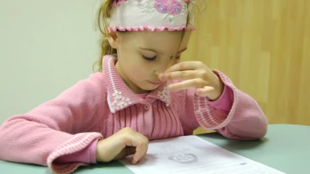 Little girl sits at table with piece of paper and reads test — Stock Video