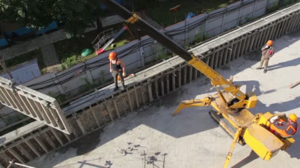 Kran hebt einen Teil der Mauer und trägt sie, mehrere Arbeiter sind in der Nähe — Stockvideo