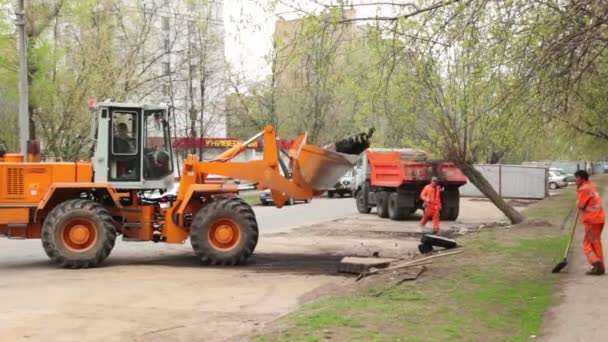 Excavatrice soulève l'asphalte, les travailleurs se tiennent près au démantèlement des petits garages — Video