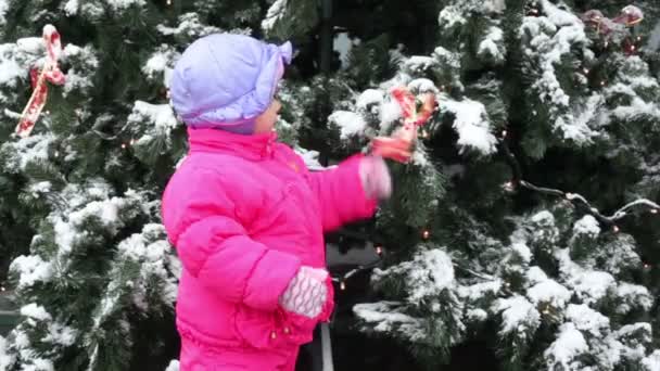 Klein meisje schudden boog lint op kerstboom bedekt met sneeuw — Stockvideo