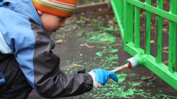 Little boy with paintbrush in hand carefully dye fence on community work day — Stock Video