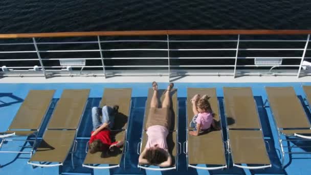 Mother with two children sunbathing and playing games on sunbed on ship deck — Stock Video