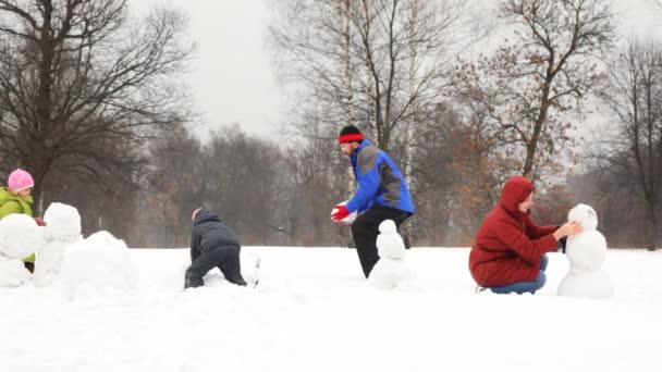 Madre con niños hacen muñeco de nieve, padre toma gran bola de nieve en invierno — Vídeos de Stock