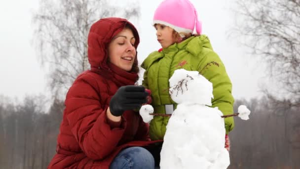 Mother with daughter, turn head in small snowman — Stock Video