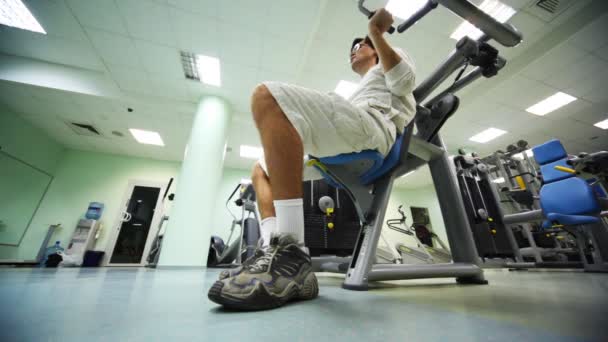 Homem faz exercitar músculos dos ombros enquanto sentado no exercitador e levanta alavancas para cima no ginásio — Vídeo de Stock
