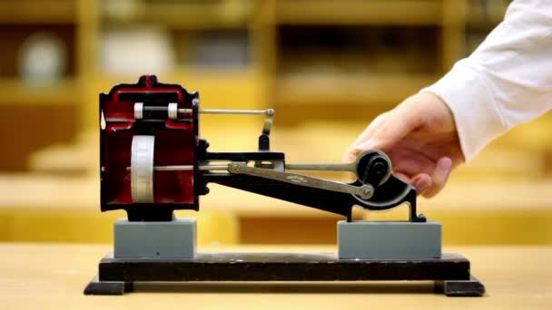 Mann dreht Modell einer Dampfmaschine auf gelbem Schreibtisch im Physikunterricht — Stockvideo