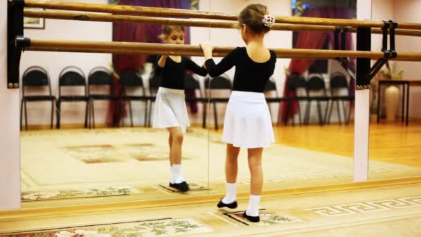 Niña hace movimientos de piernas de ballet mientras se enfrenta al espejo en la sala — Vídeo de stock