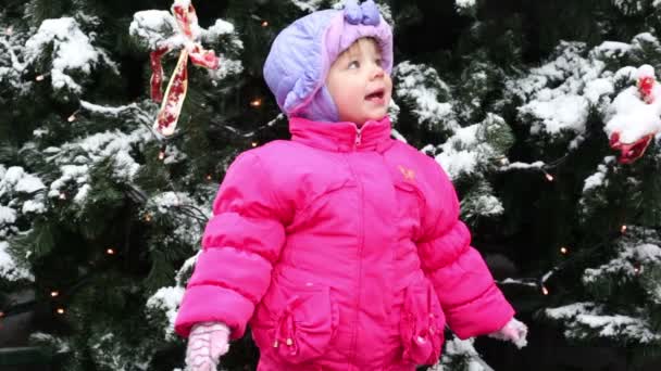 Menina fica e olhar para a frente da árvore de Natal coberta de neve — Vídeo de Stock